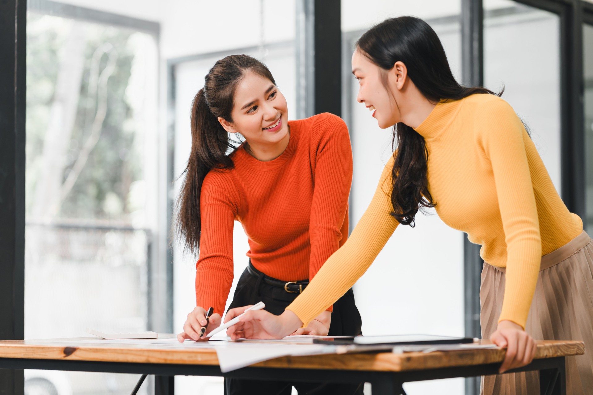 Collaborative women working together in modern office, sharing ideas and discussing plans with enthusiasm. Their vibrant outfits add energy to workspace