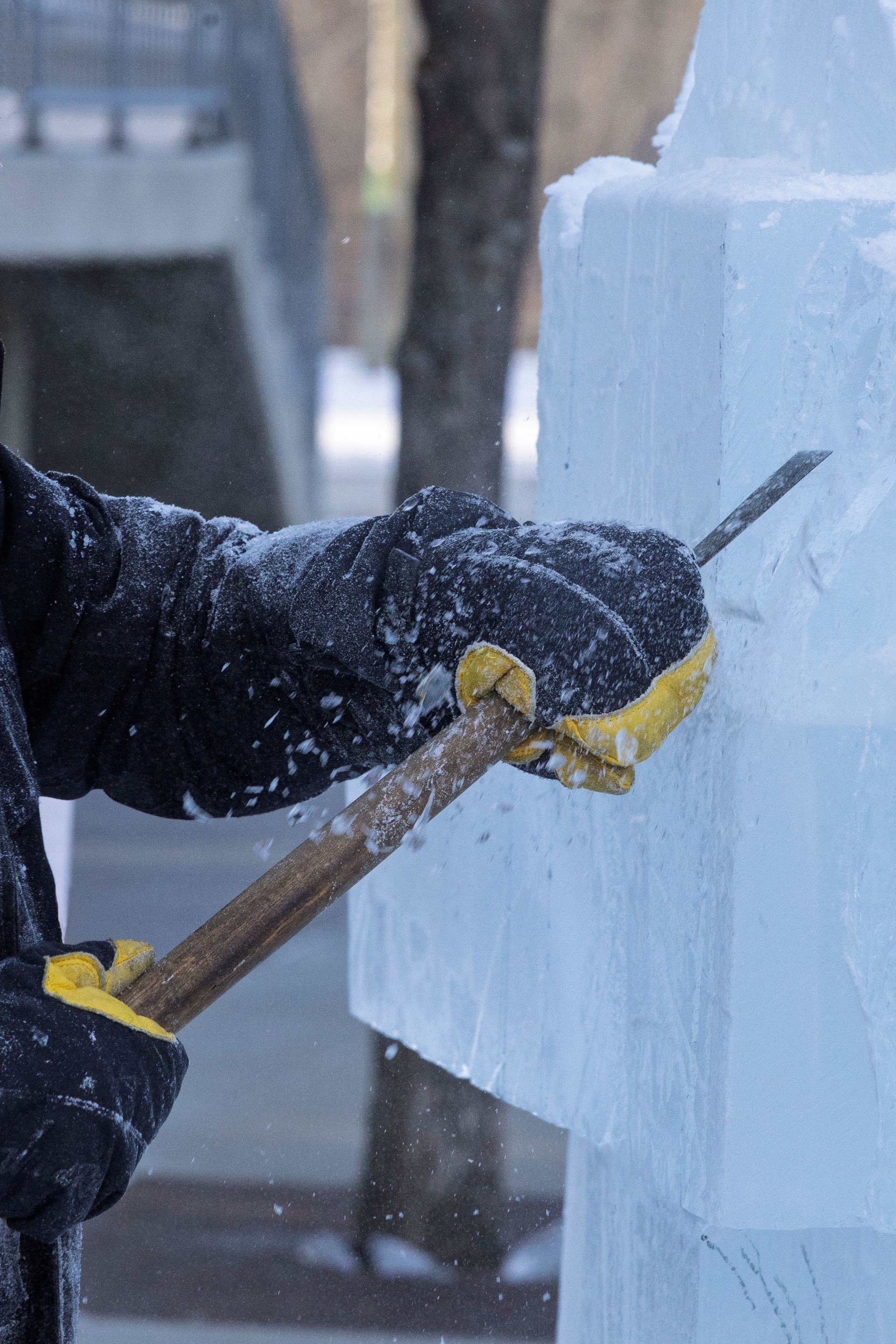 Outdoor winter image of an unrecognizable person wearing black gloves and holding a hand tool while sculpting an ice block.